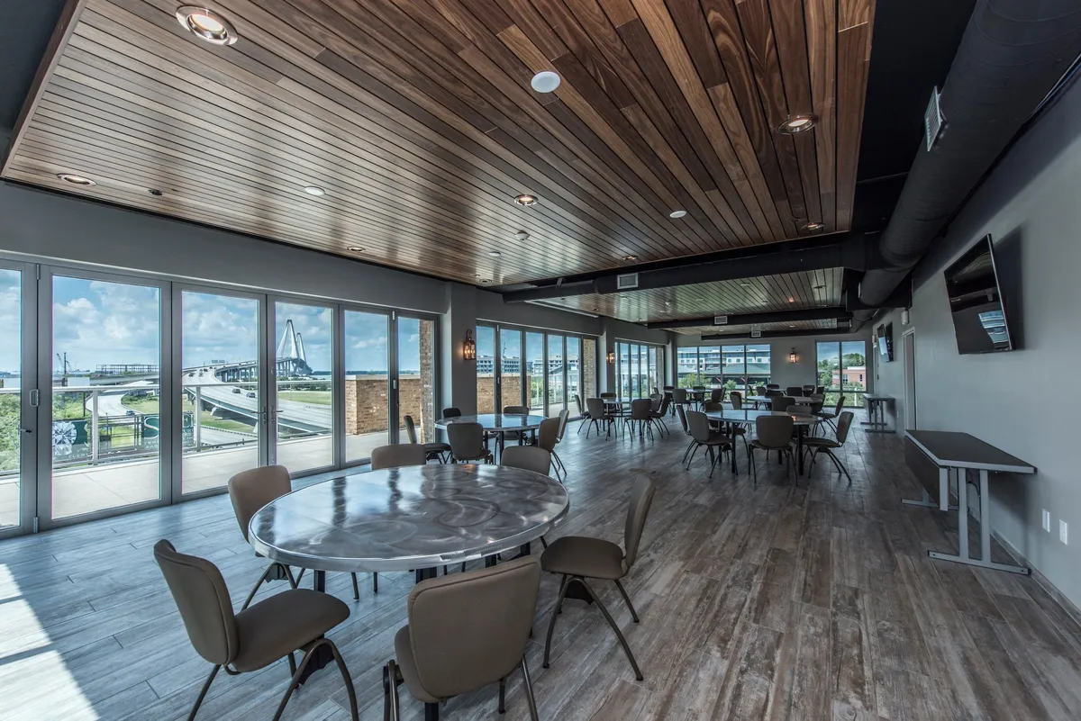A welcoming dining area with large windows offering scenic views, round tables set for meals, and a wooden ceiling that adds warmth to the space. The arrangement encourages social gatherings and relaxed dining experiences.