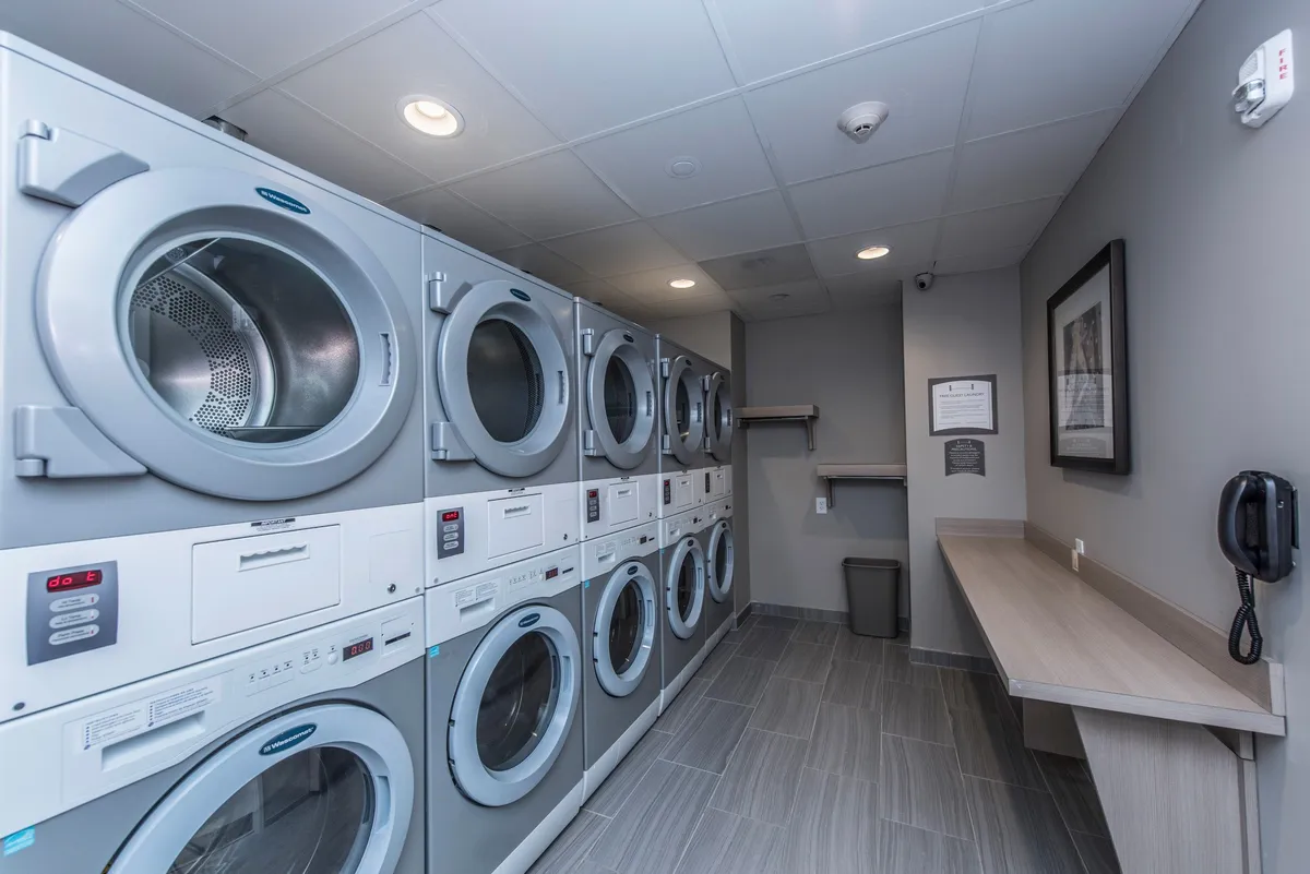 A neatly organized laundry room with several washing machines lined up along the wall, a folding table, and shelving for laundry supplies. The space is bright and practical, providing convenient amenities for guests.