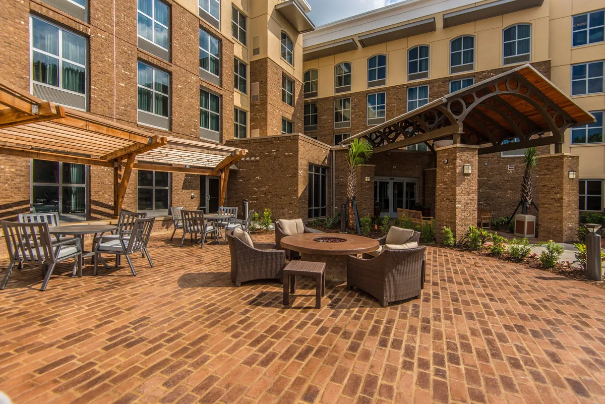 An outdoor brick patio with a central fire pit and ample seating is featured here. The area is designed for social gatherings, outdoor dining, and cozy relaxation, with a warm, welcoming mood as the sun sets.
