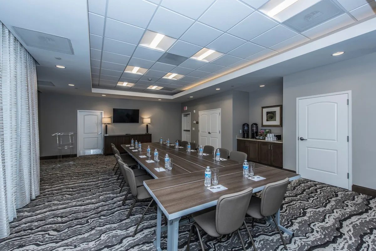 A modern, purpose-built interior meeting room with a long table, water bottles, a wall-mounted screen, and chairs arranged for collaboration. The setting is bright, functional, and ideal for business meetings, workshops, or team brainstorming, clearly illustrating the property’s business-friendly facilities.