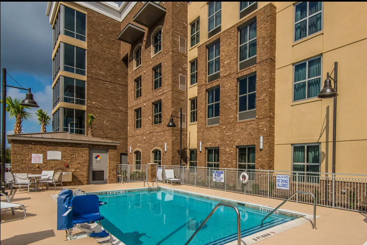 This exterior image showcases the hotel’s sparkling outdoor swimming pool surrounded by comfortable lounge chairs and the building’s facade. Hints of social activity and relaxation are present, with inviting poolside spaces ideal for unwinding after a productive day. The image is set in a relaxed, sunset ambiance, highlighting the property’s leisure amenities.