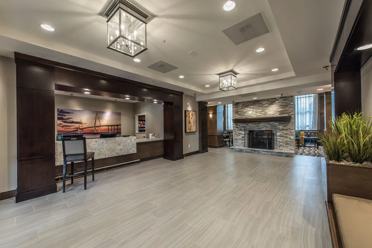 The lobby area showcases a welcoming front desk, comfortable seating, a cozy fireplace, and curated artwork on the walls, creating a warm and inviting ambiance. The space is ideal for making a memorable first impression and for guests to relax, socialize, or plan their Charleston adventures.