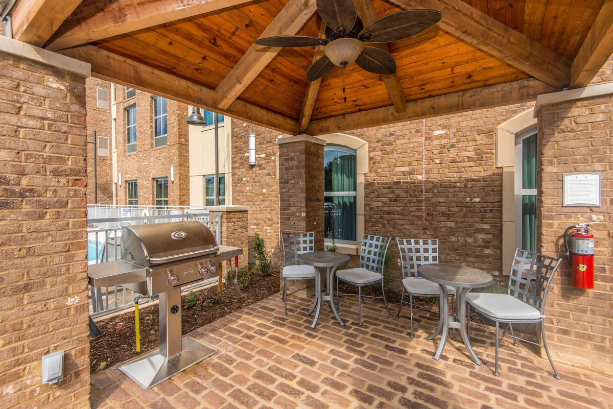 This exterior image features a covered patio area with a wooden ceiling, outdoor seating, and a grill. The scene evokes a relaxed, sociable atmosphere, perfect for guests who want to unwind after a day exploring Charleston or the nearby beaches. The outdoor setup suggests spaces for al fresco dining, informal gatherings, or simply relaxing with a drink in hand as the sun sets.