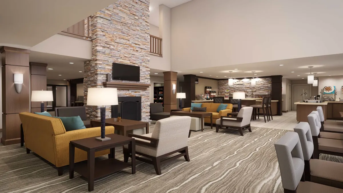 A cozy common area featuring a stone fireplace, ample seating, stylish lighting, and a kitchenette area nearby. The layout suggests a shared guest space ideal for relaxing or taking care of practical needs such as laundry.